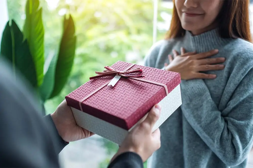 Person handing a wrapped gift box to a smiling woman