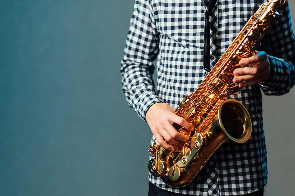 Person holding an alto saxophone against a blue background