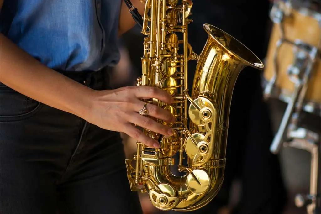 Person holding a gold saxophone beside a drum kit