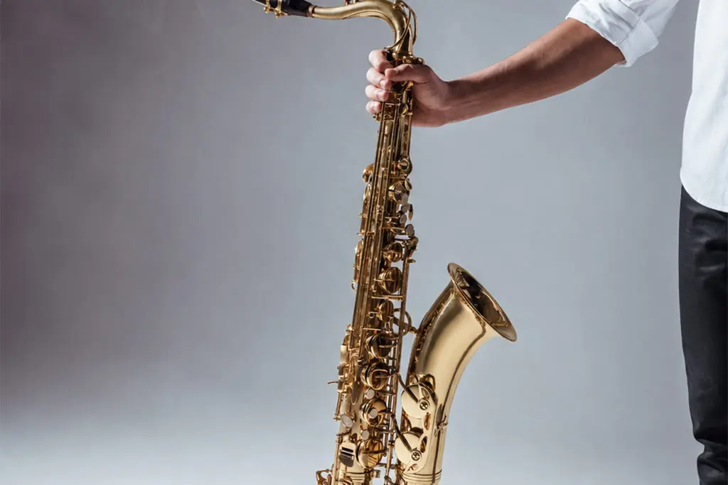 Cropped person holding a tenor saxophone against a grey background
