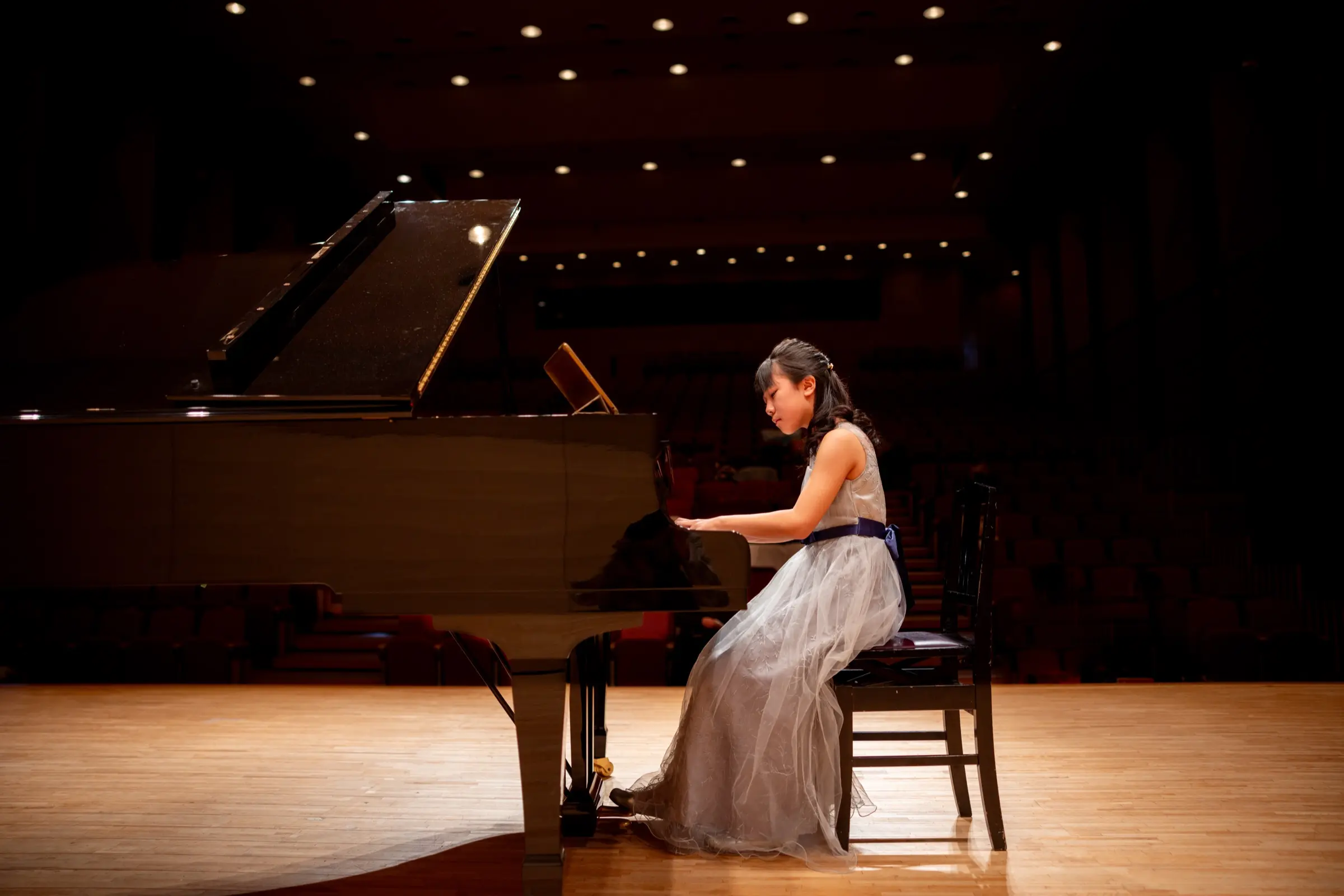 Young pianist performing on a grand piano on a concert stage.