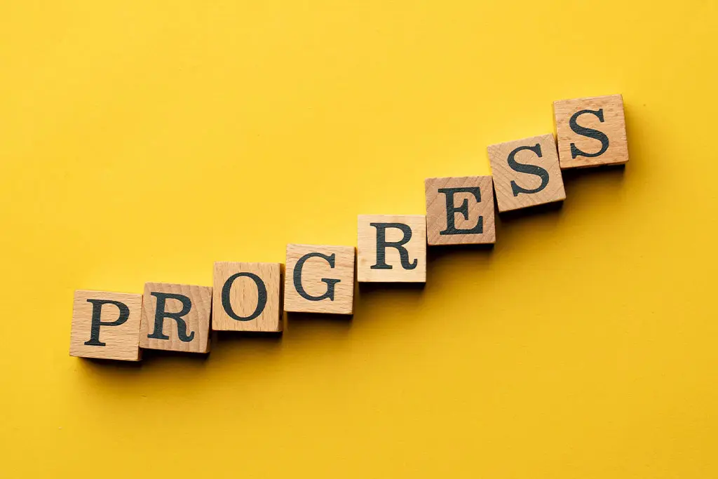 Wooden letter blocks spelling progress on a yellow background