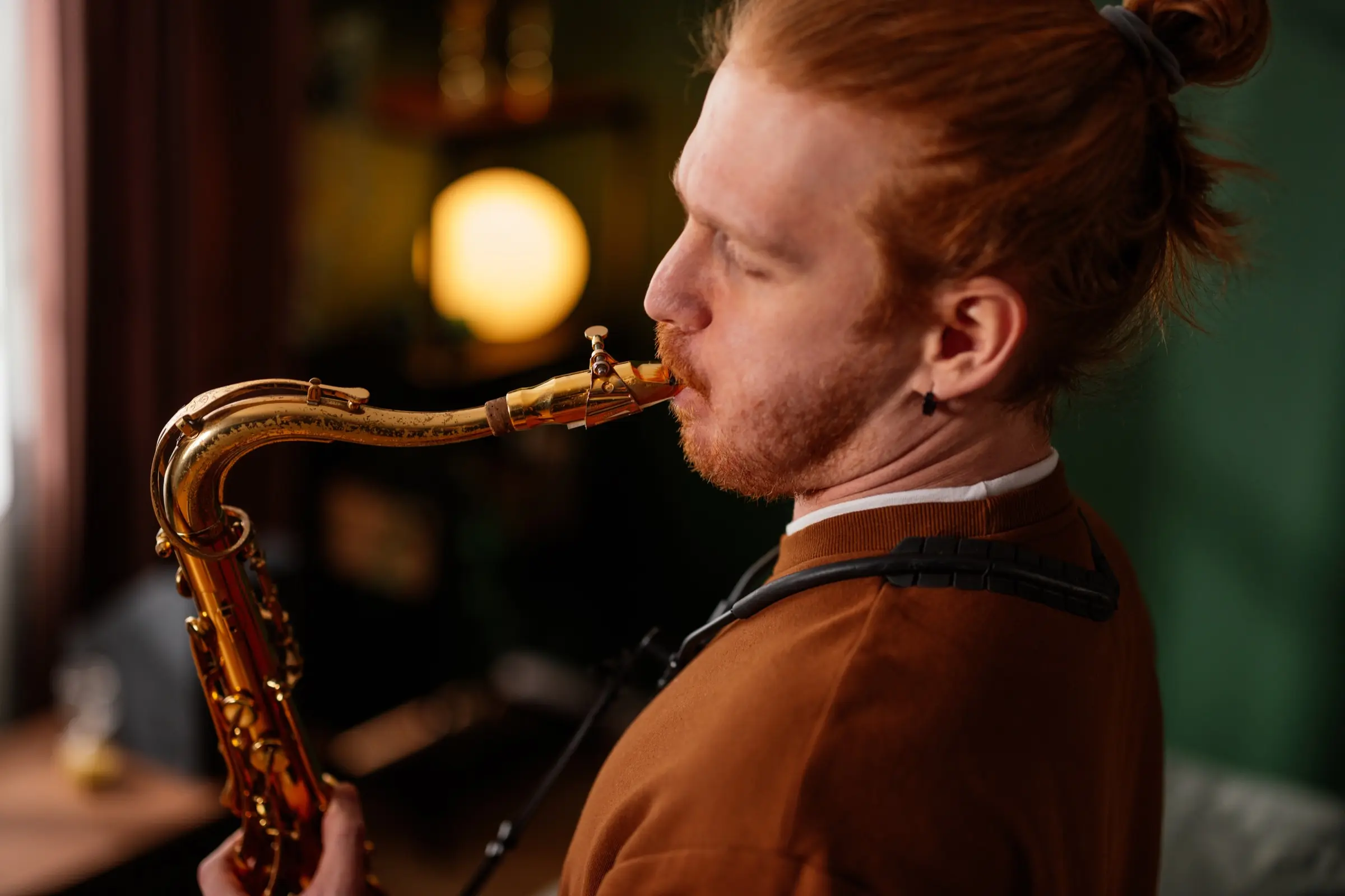 Man with red hair playing the saxophone in a dimly lit room.