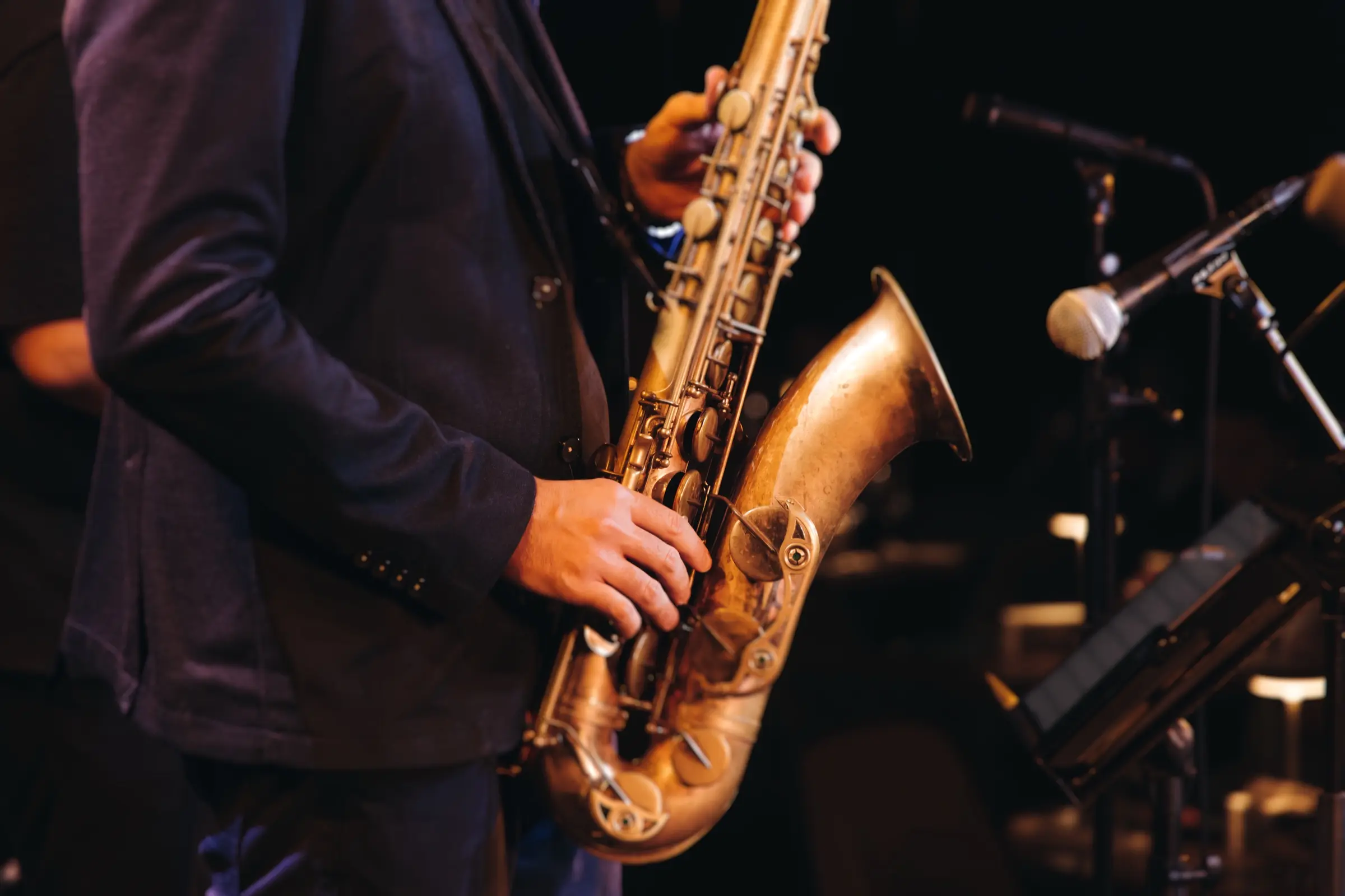 Close-up of a saxophonist playing on stage beside a microphone.