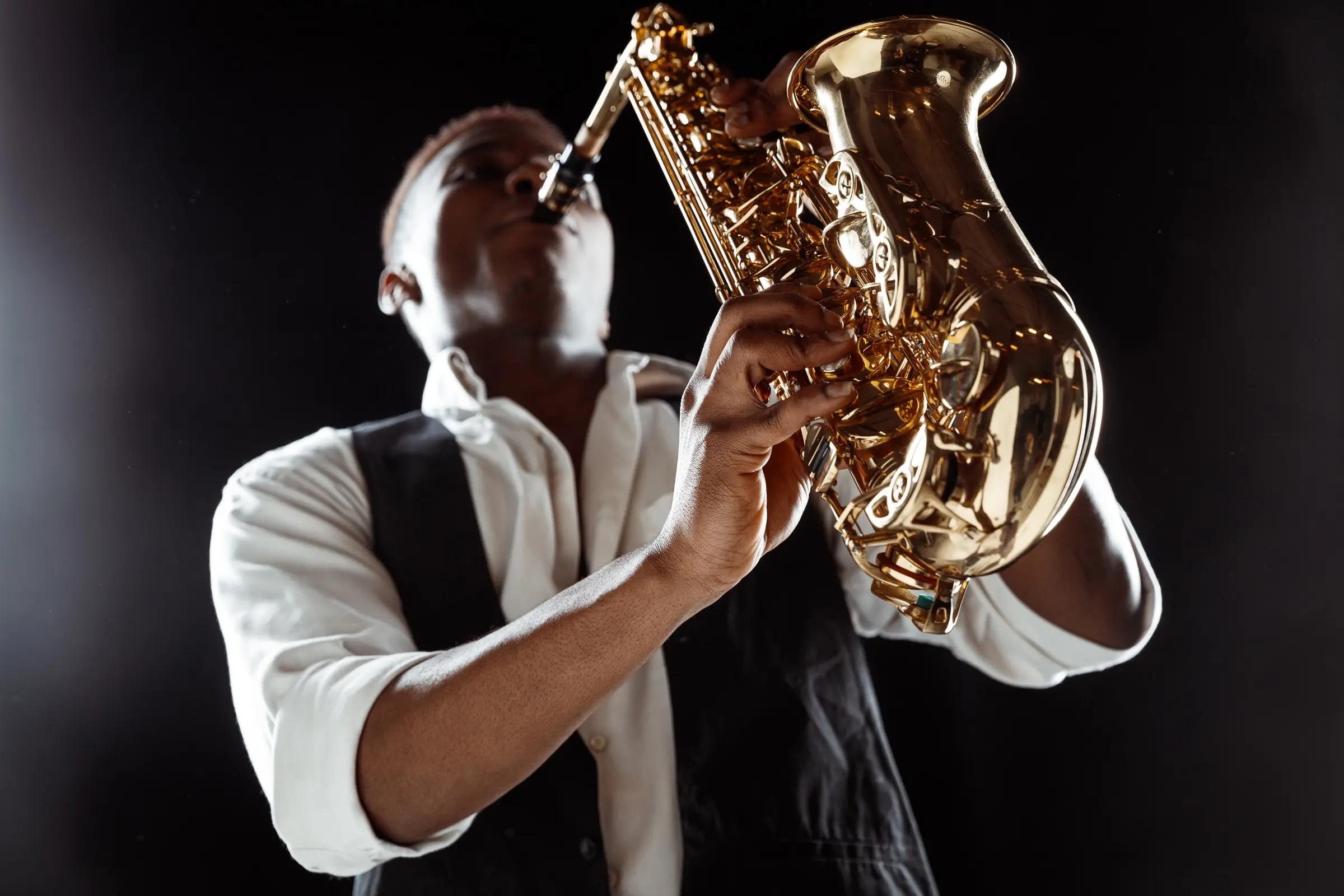 Saxophonist in a waistcoat playing against a dark background.