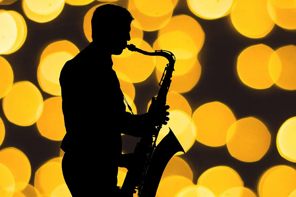 Silhouetted saxophonist playing against warm blurred lights