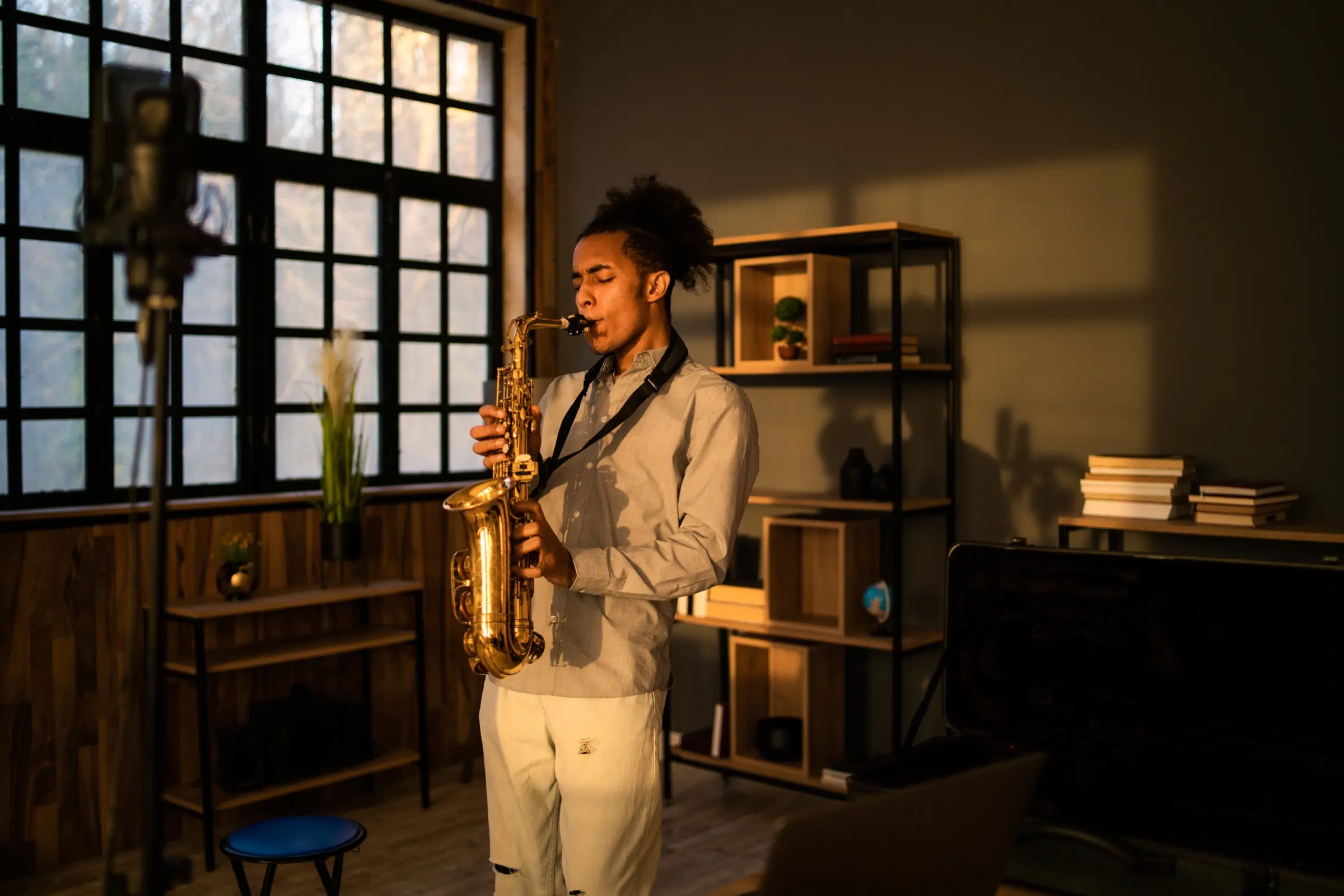 Saxophonist dressed in white rehearsing alone in a room with tall windows.