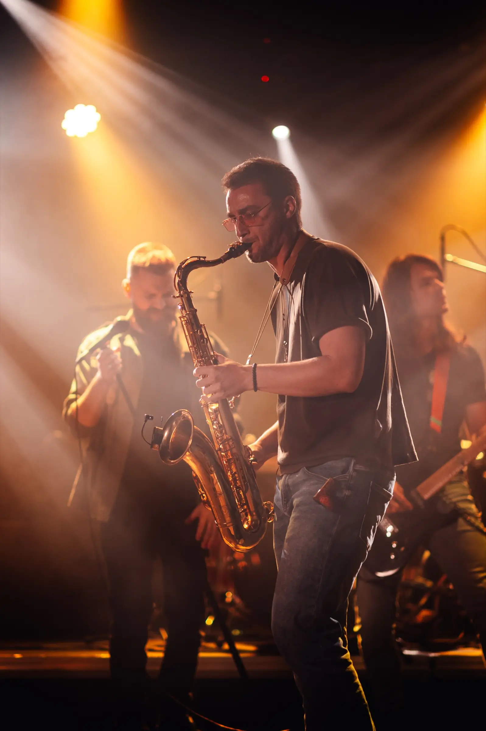 Saxophonist performing with a band under warm stage lights.