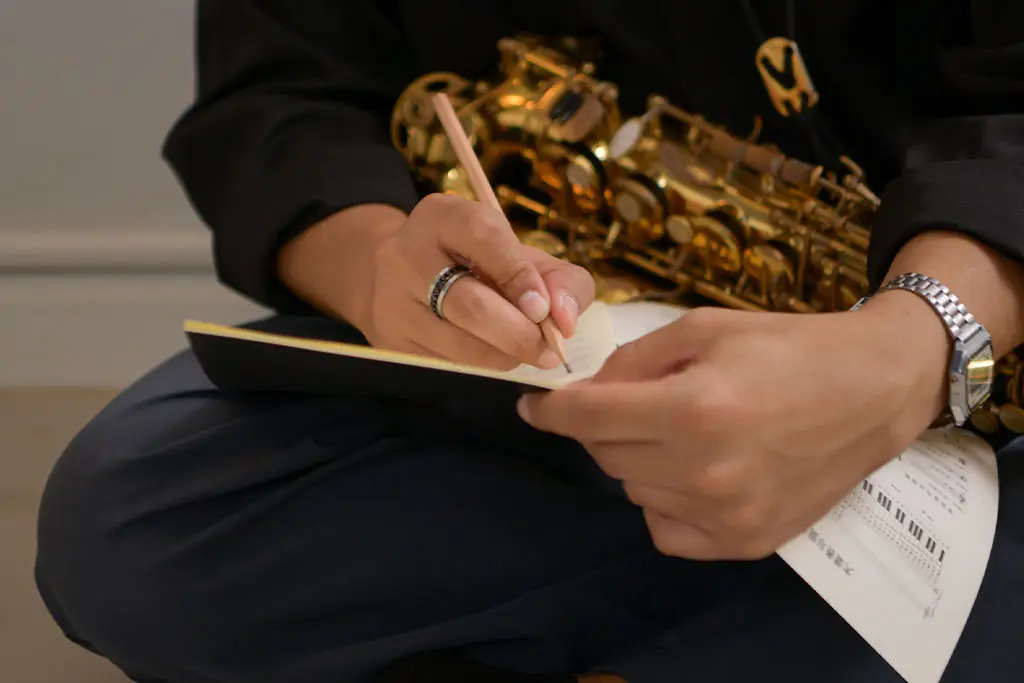 Close-up of saxophonist writing in a notebook with sheet music visible