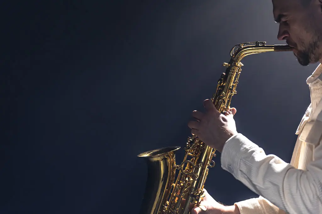 Side profile of a man playing saxophone against a dark background