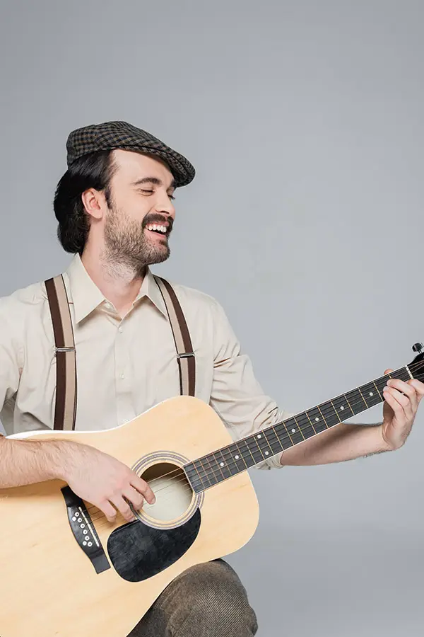 Smiling man in a flat cap playing an acoustic guitar