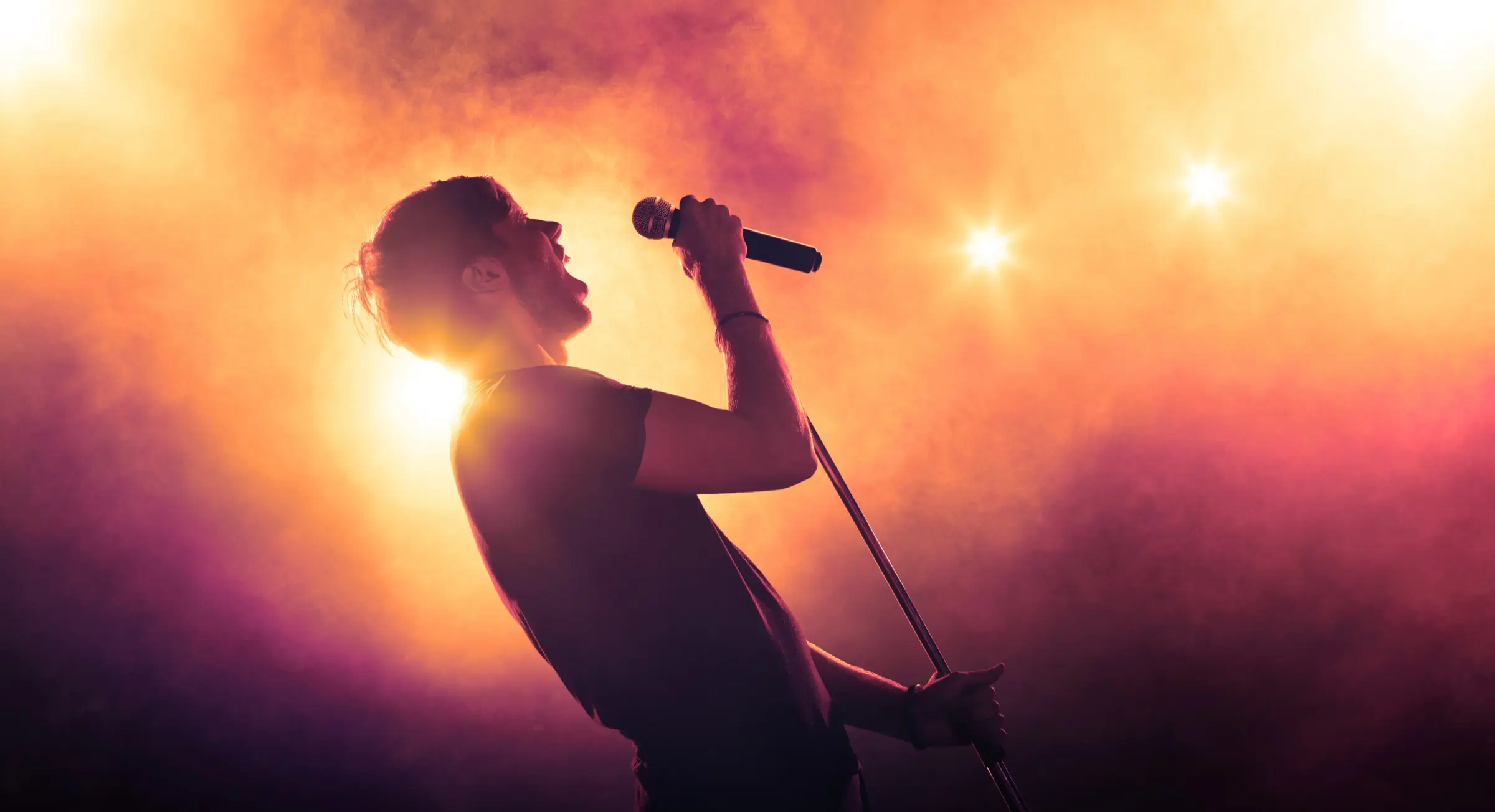 Singer silhouetted against stage lights, holding a microphone.