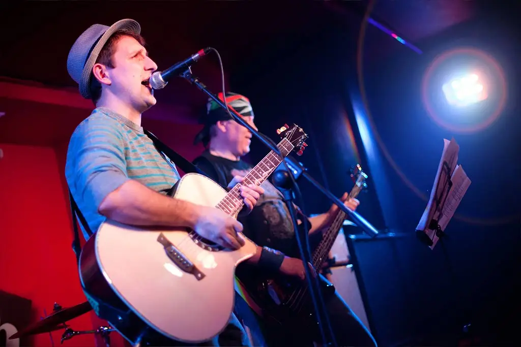 Singer playing acoustic guitar on stage with a bassist