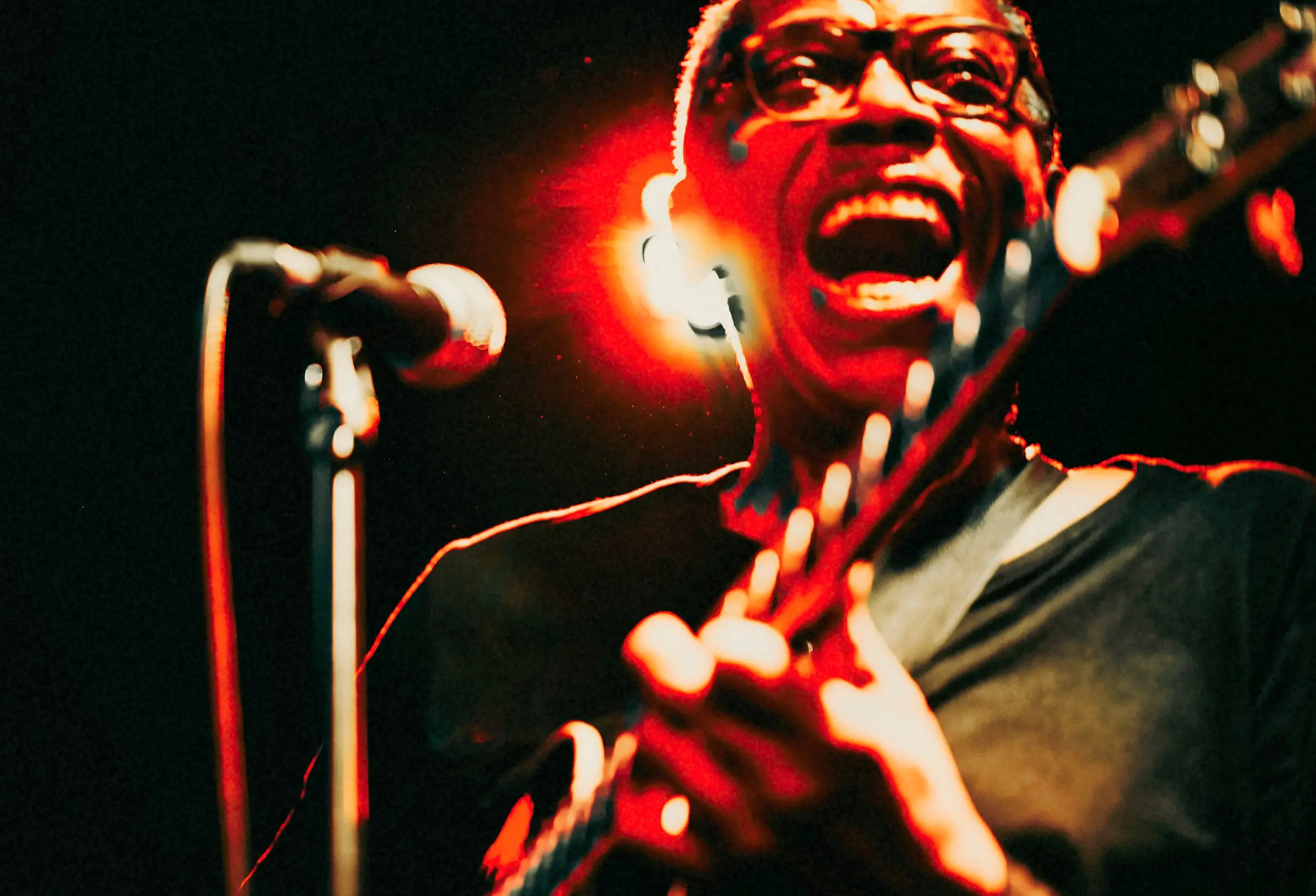 Singer in glasses performing with a guitar under red stage light.