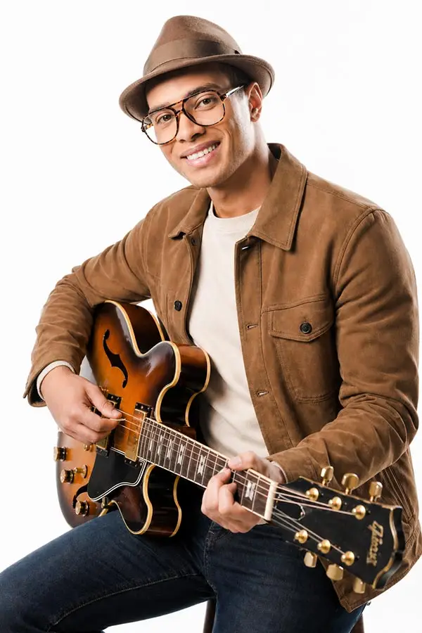 Smiling man in a brown hat playing a semi-hollow electric guitar
