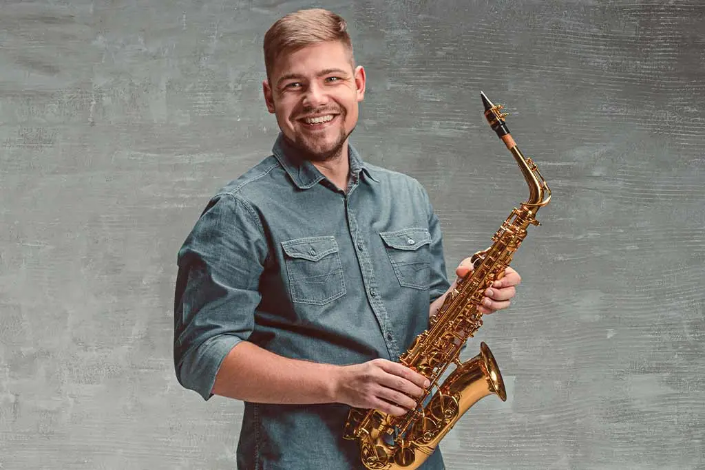 Smiling man in a denim shirt holding an alto saxophone