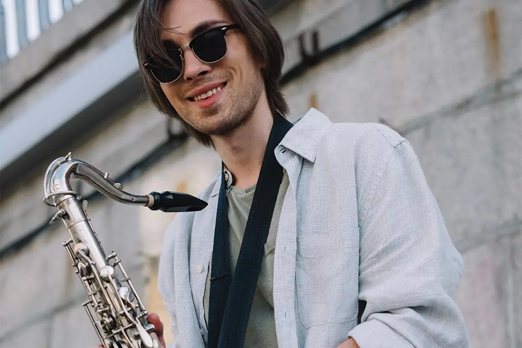 Smiling man in sunglasses holding a saxophone outdoors