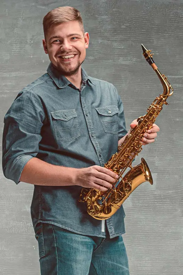 Smiling man in a denim shirt holding an alto saxophone