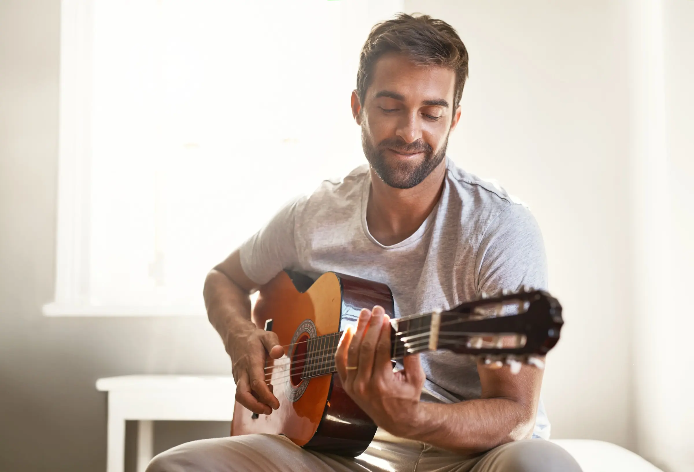 Smiling man playing a classical guitar in a bright room.
