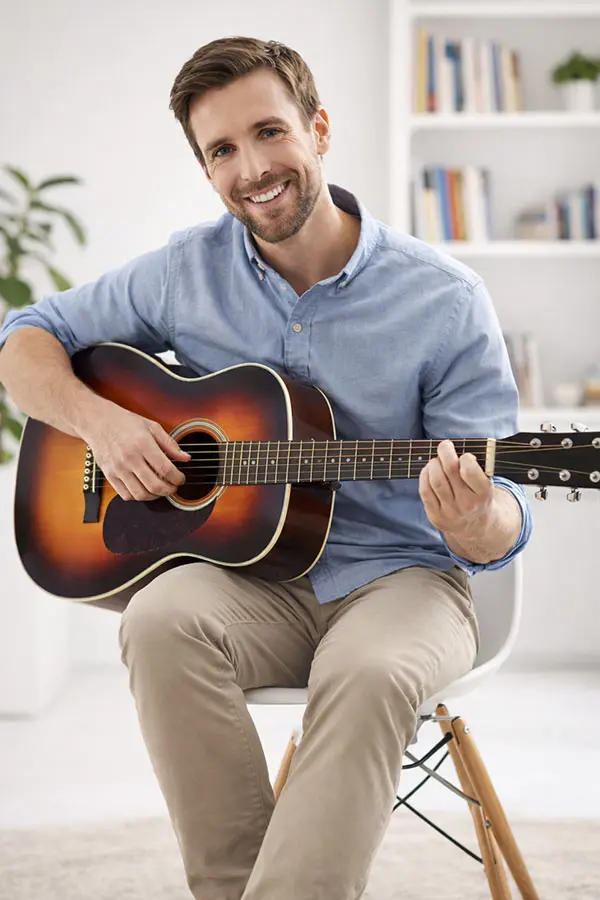 Smiling man in a pale blue shirt playing sunburst acoustic guitar