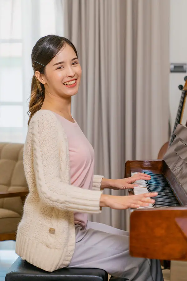 Smiling woman in a cream cardigan playing an upright piano