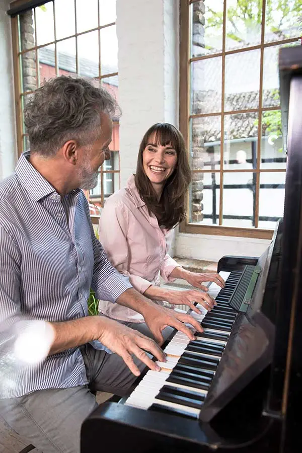 Man in a striped shirt and woman playing piano by windows