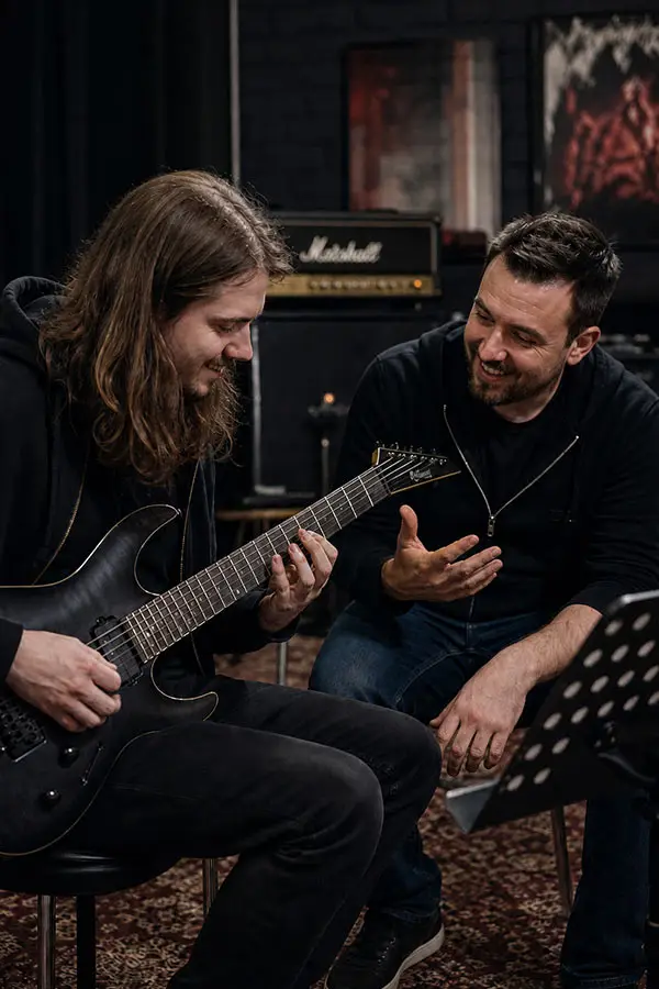 Man playing electric guitar while another man gives guidance