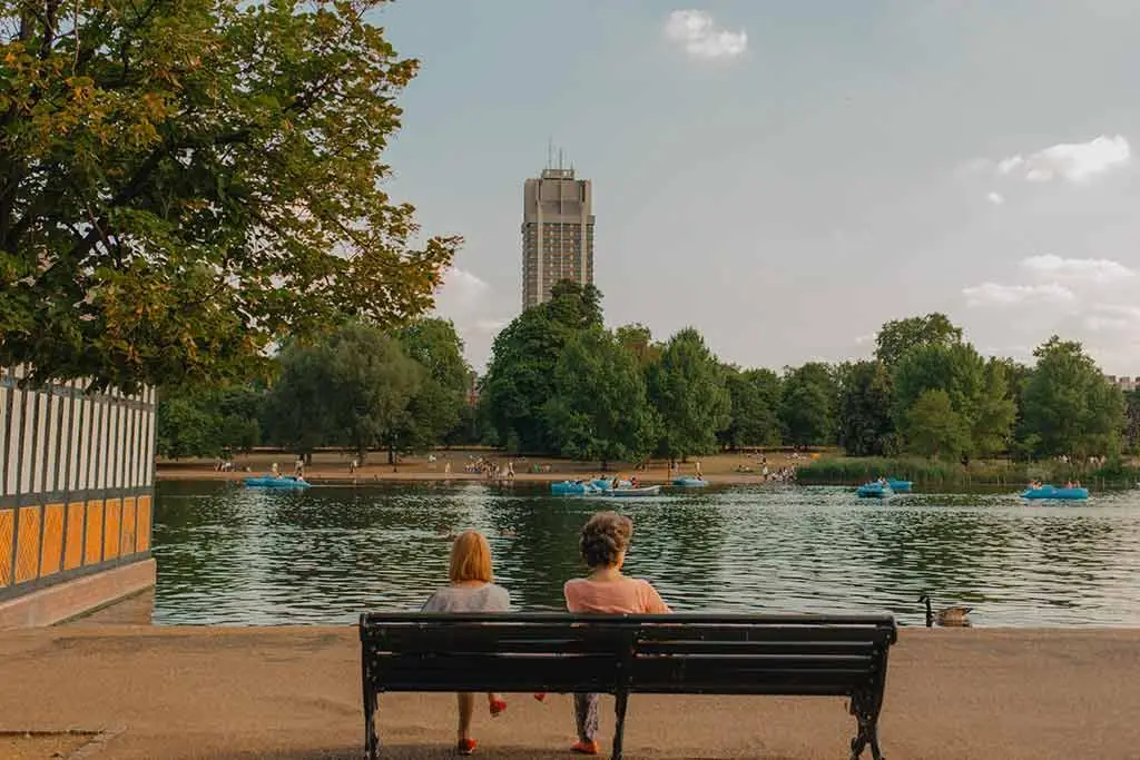 Two people sitting on a bench beside a park lake