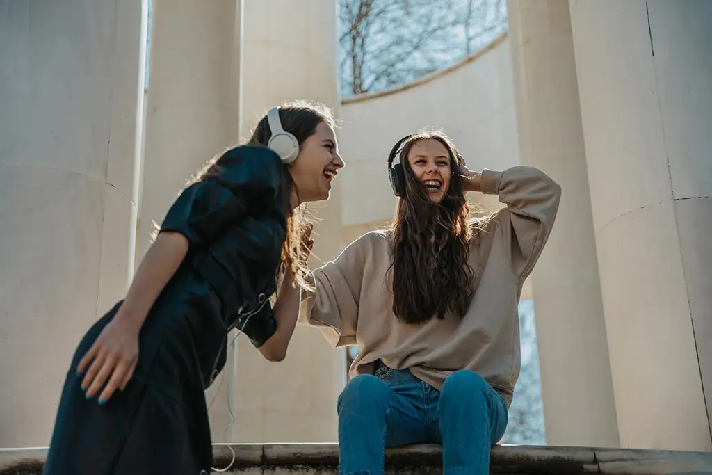 Two women laughing while wearing headphones outdoors