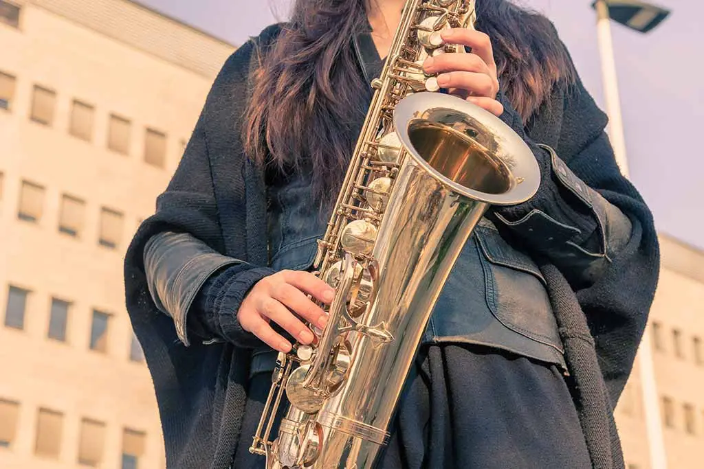 Woman in a black coat holding a saxophone outdoors
