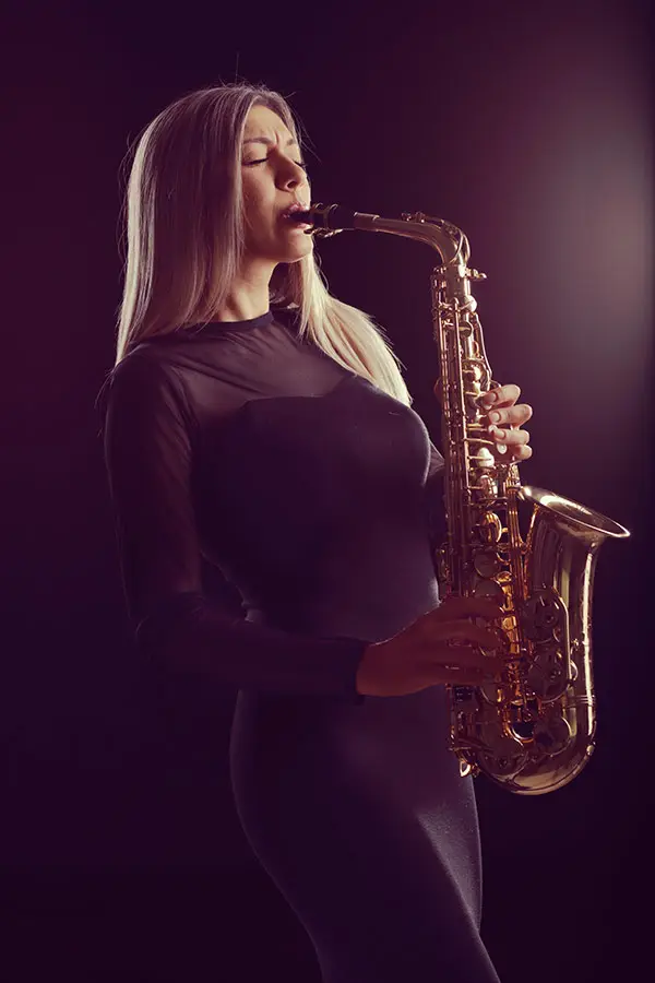 Woman in a black dress playing saxophone against a dark background