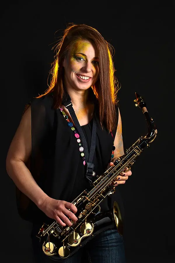 Smiling woman with an alto saxophone against a dark background