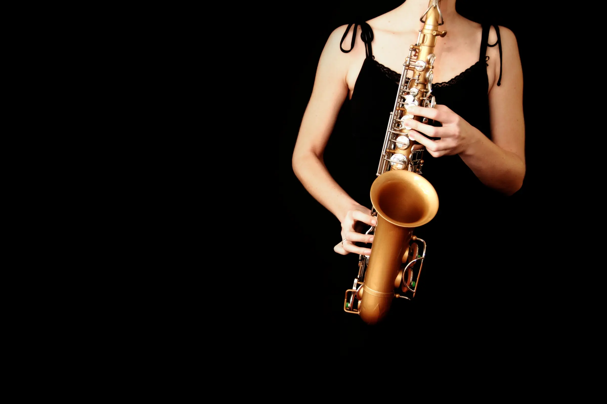 Woman in a black dress holding a saxophone against a black background.