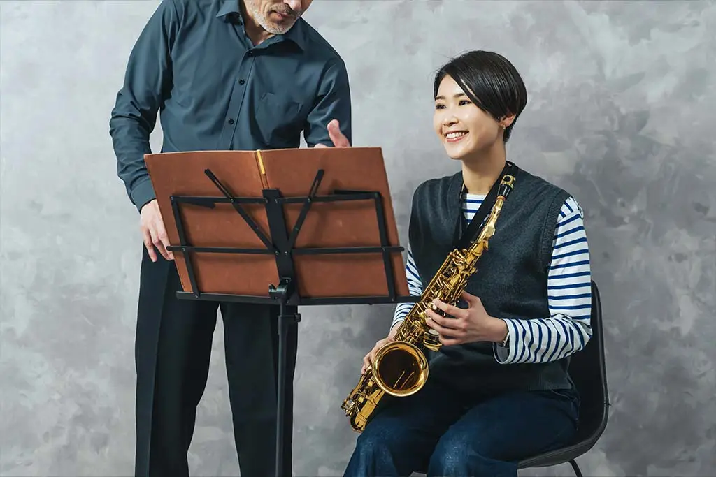 Woman holding an alto saxophone beside a man and music stand