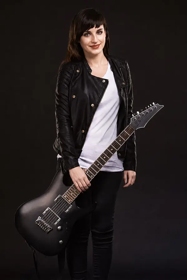 Woman in a white shirt holding a black electric guitar