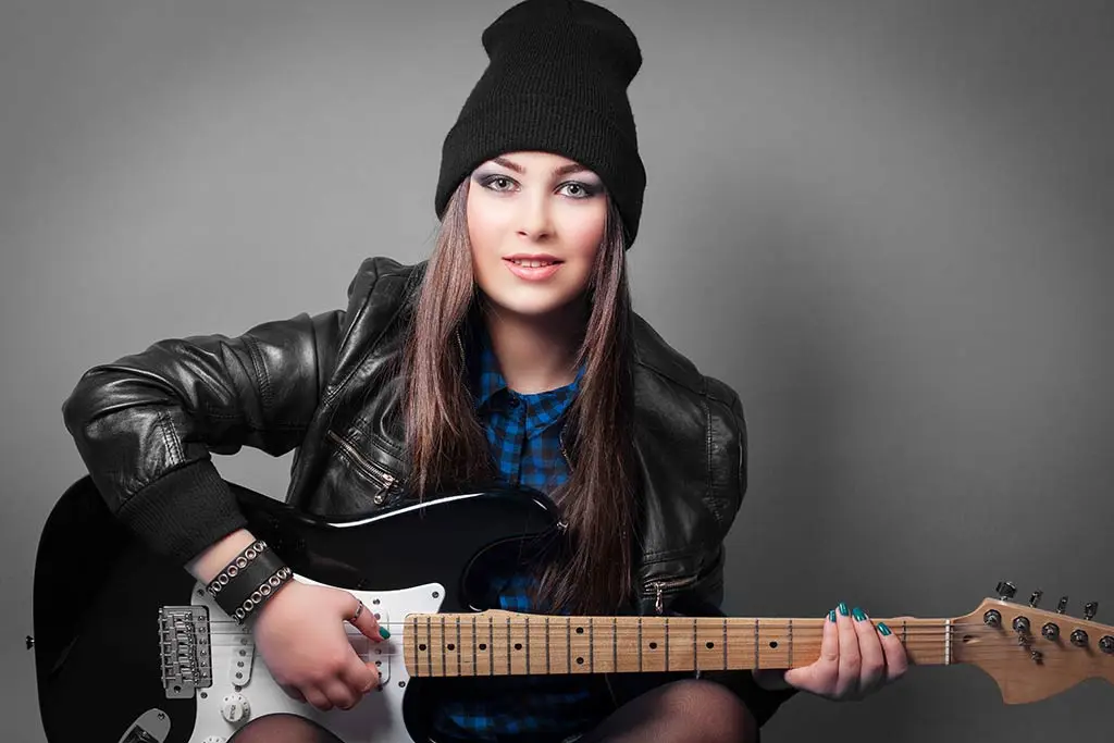 Woman in a beanie playing a black electric guitar