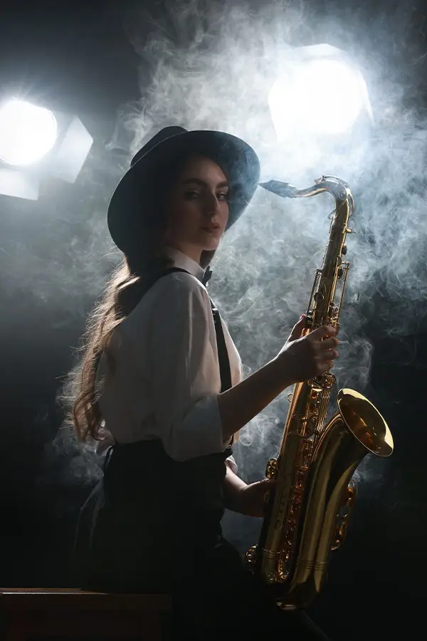 Woman in a hat holding a saxophone in smoky light