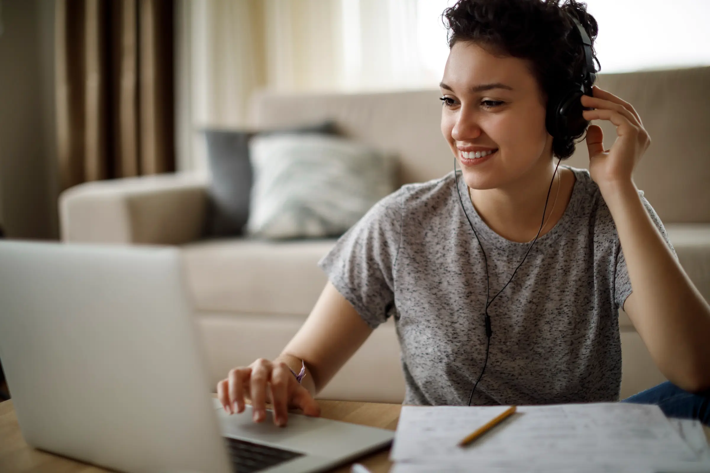 A student with headphones studying at a laptop with notes beside her