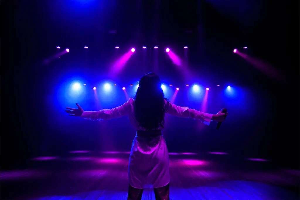 Woman on stage with arms outstretched holding a microphone