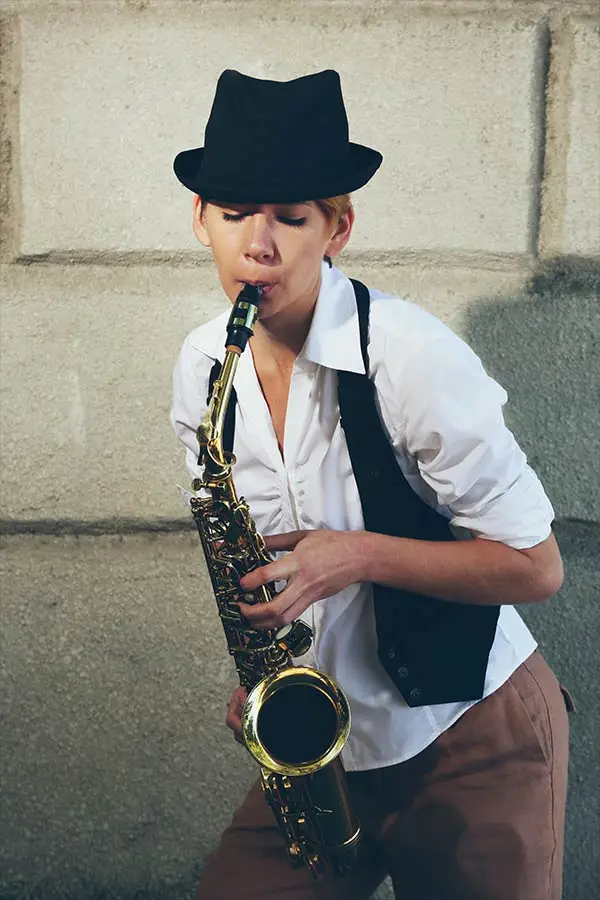 Woman in a black hat playing an alto saxophone by a wall