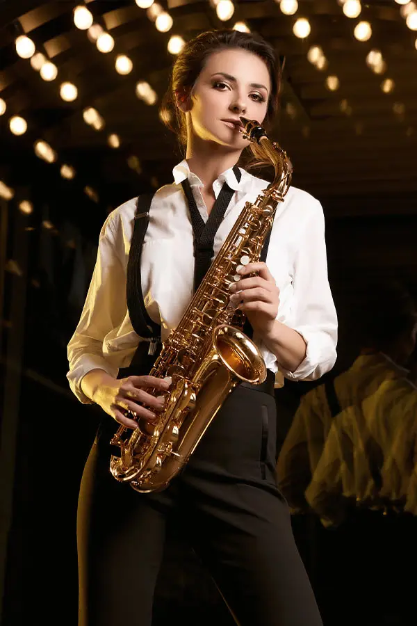 Woman playing an alto saxophone beneath rows of warm bulb lights