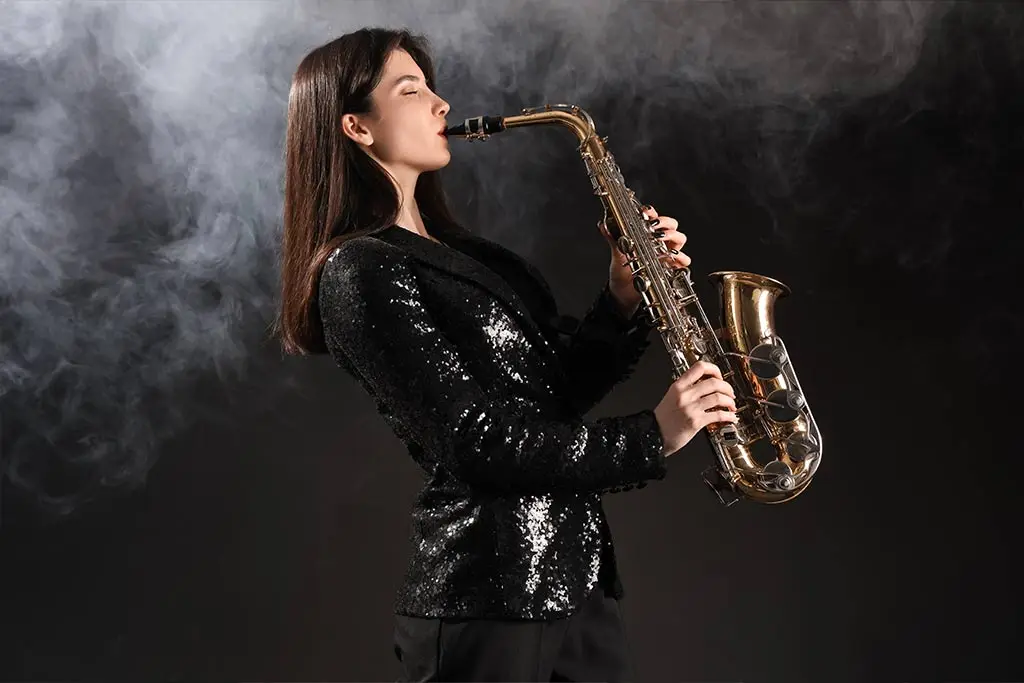 Woman in a black sequin jacket playing an alto saxophone in smoke