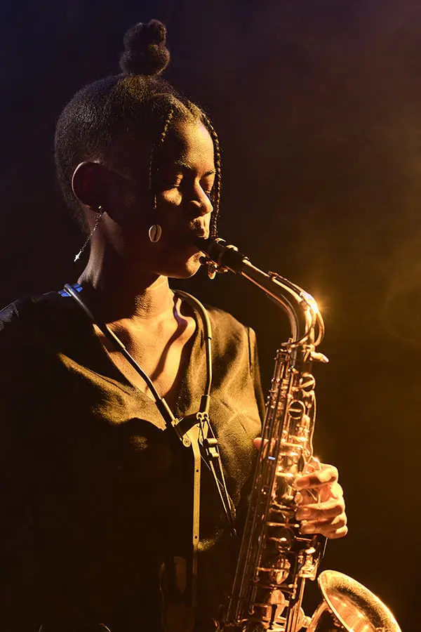 Woman with a topknot playing an alto saxophone in warm stage light