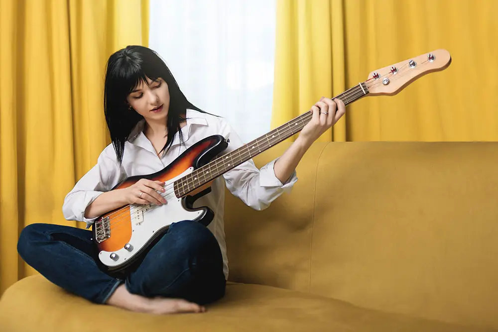Lady playing the bass guitar - sitting on a yellow sofa with crossed legs