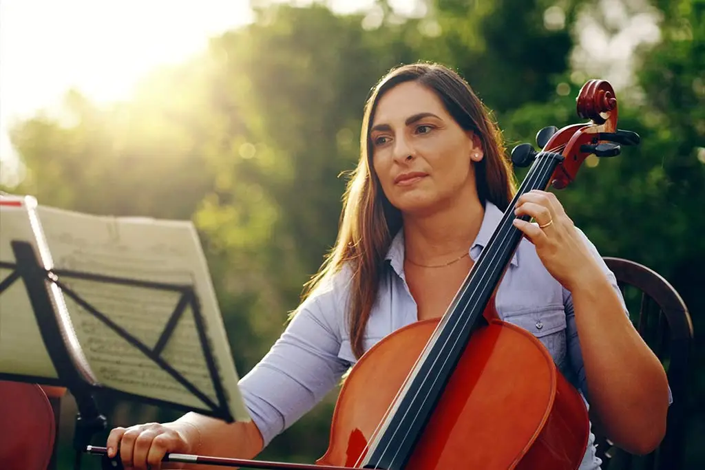 Woman playing cello beside a music stand outdoors