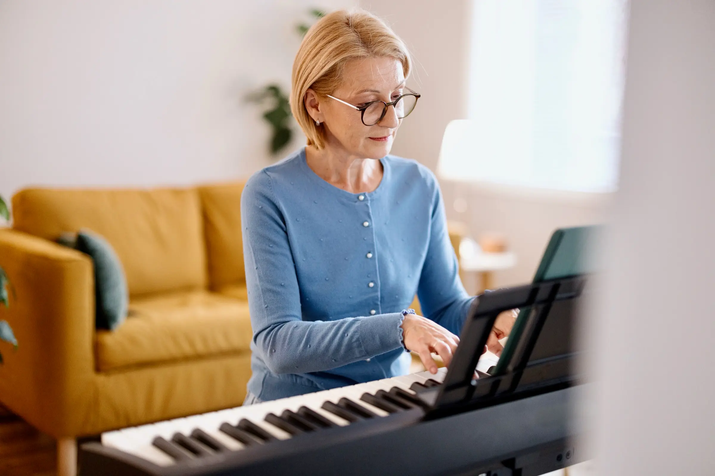 Woman in glasses playing a digital piano in her living room.
