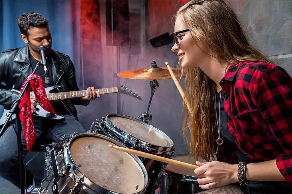 Woman playing drums while man playing guitar