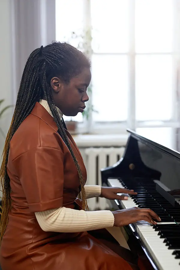 Woman in an orange dress playing a grand piano by a window