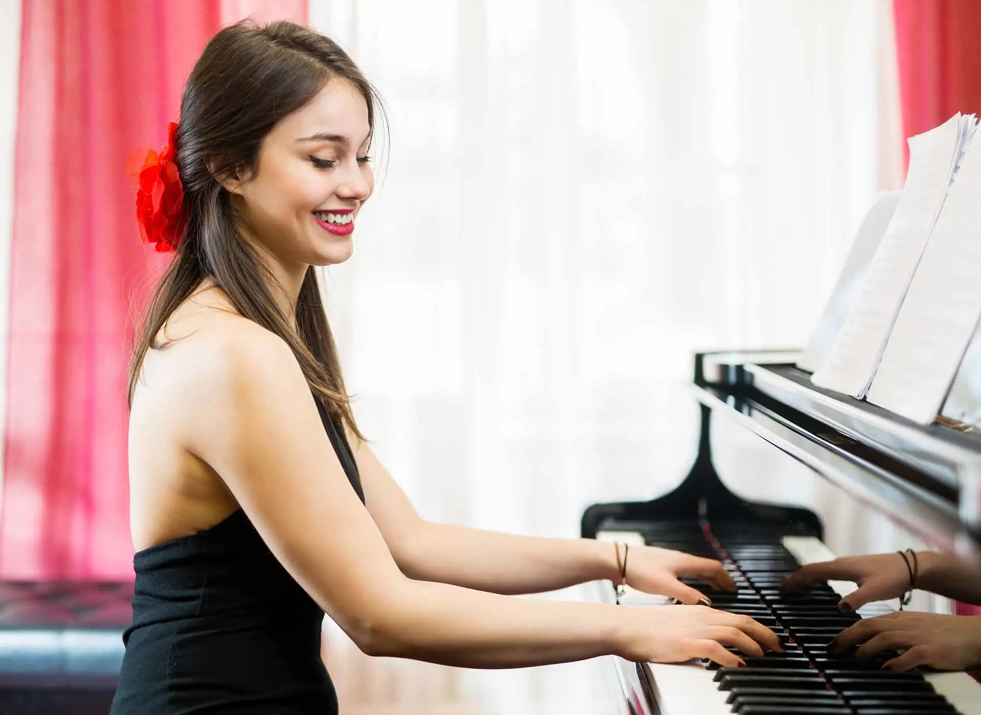 Smiling woman playing a grand piano beside red curtains