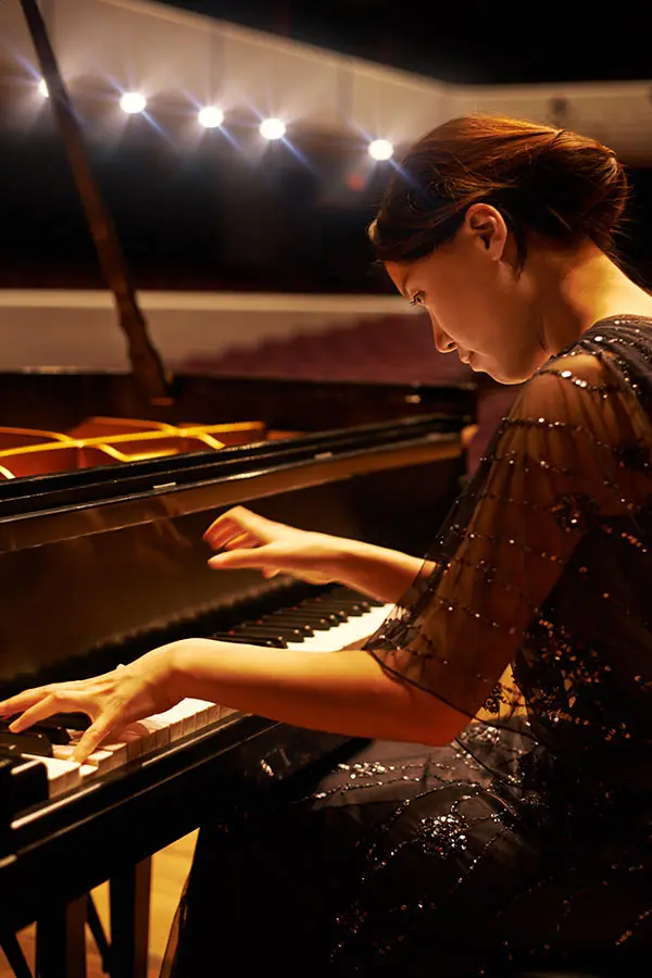 Woman playing a grand piano under warm stage lights